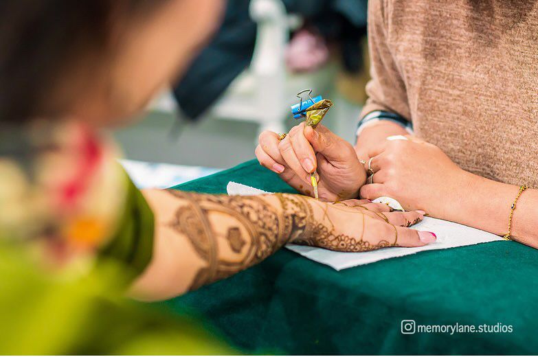 Nazia drawing henna on a guest's hand at a mehndi event