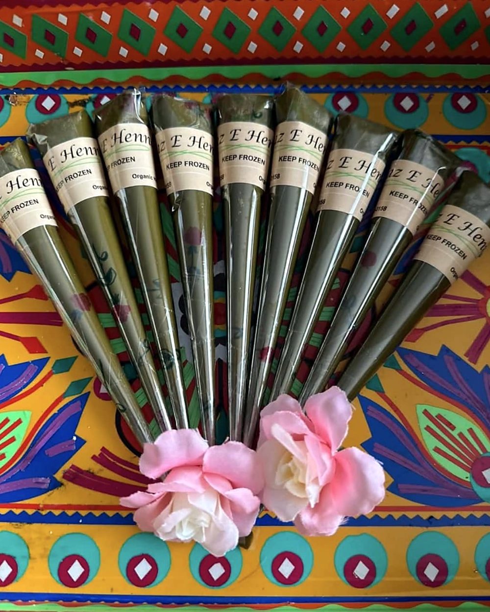 A row of labelled Naz-e-Henna henna cones with pink roses on a colourful cloth